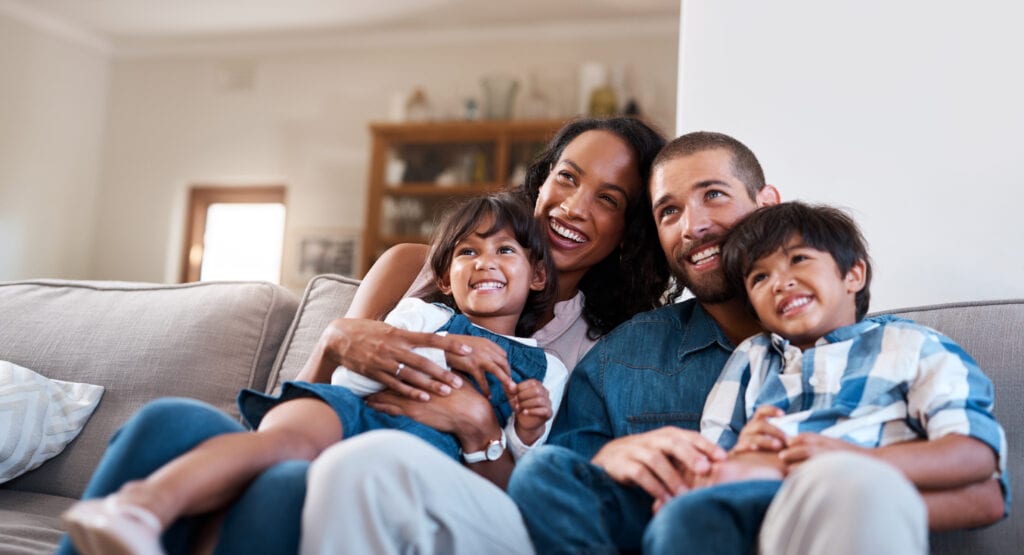Image of happy family with young daughter and son, mother and father sitting on sofa and watching CDE lightband digital services