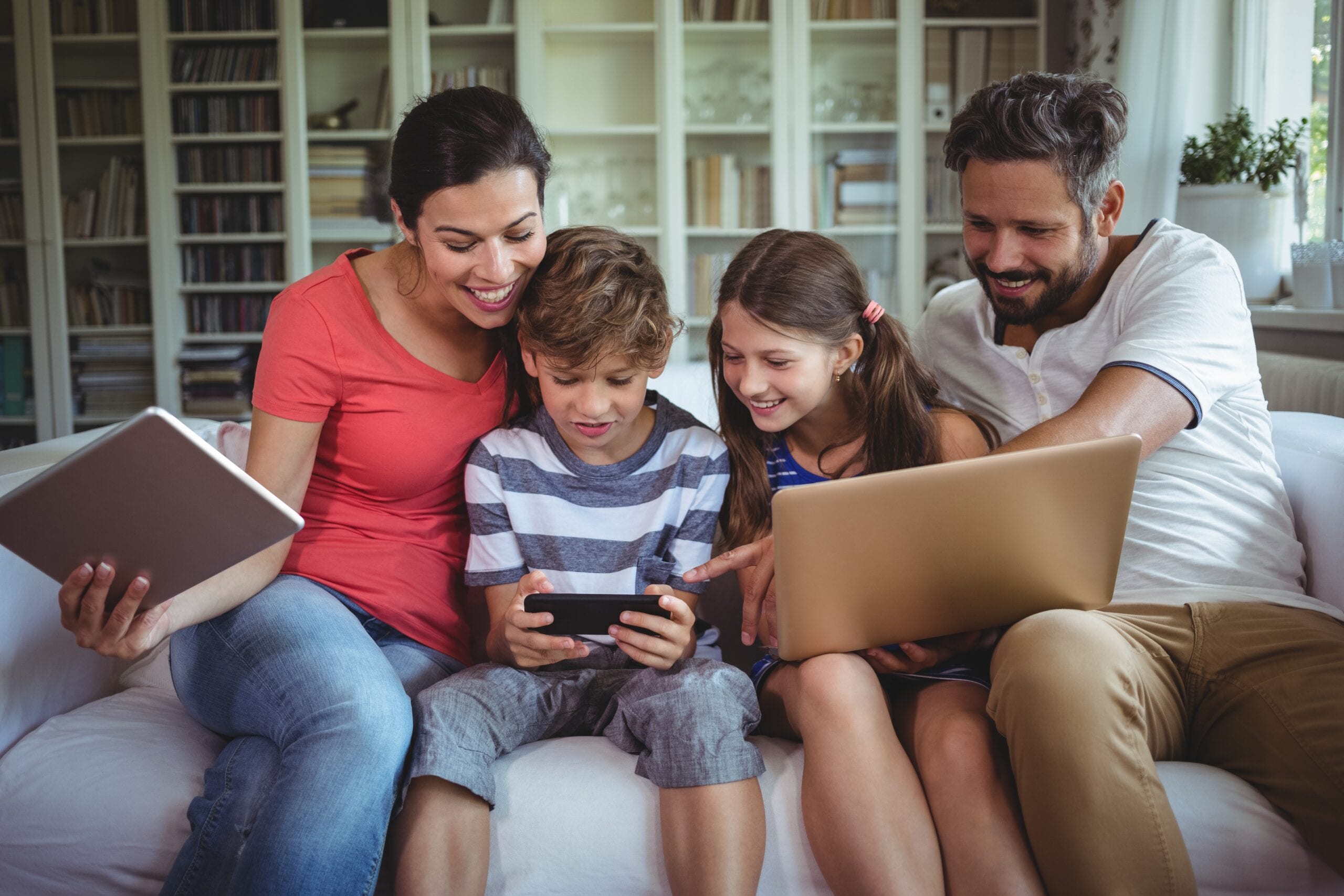 Image of whole family in living room, enjoying a variety of CDE Lightband Internet services on their tablet, phone and laptop computer