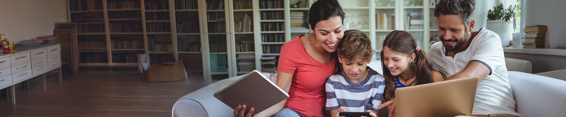 Image of whole family in living room, enjoying a variety of CDE Lightband Internet services on their tablet, phone and laptop computer
