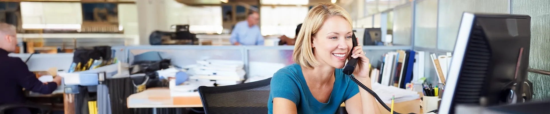 Photo of woman working in office setting on corded phone using voice services