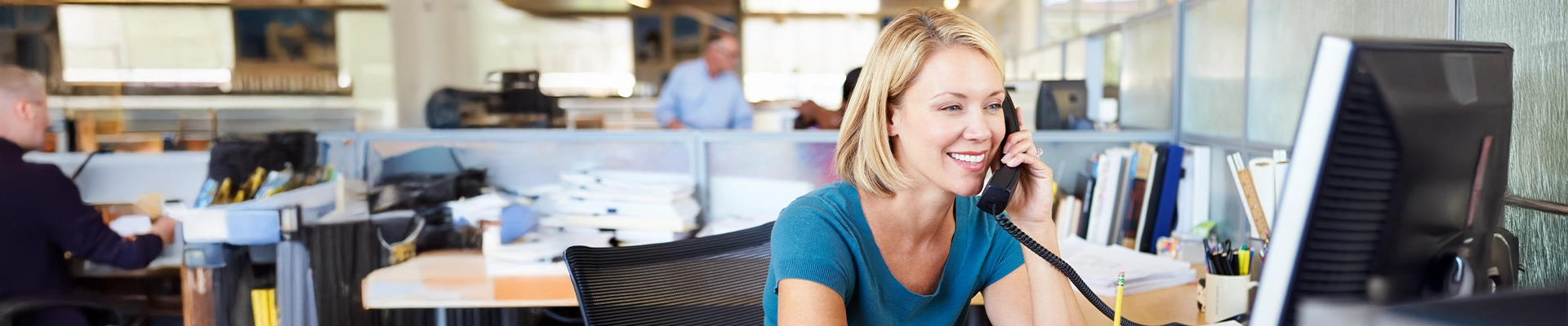 Photo of woman working in office setting on corded phone using voice services