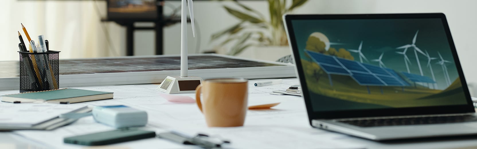 An image of a desk with a laptop, computer, coffee, cup, and model of wind turbine for wind energy